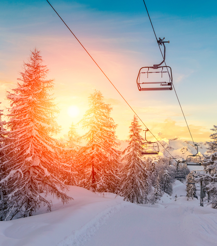 Sun sets behind ski lifts on snowy mountain