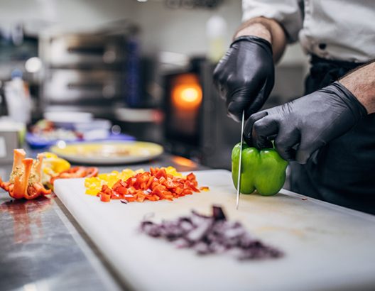 Chef in black latex gloves cutting vegetables in his kitchen in restaurant.