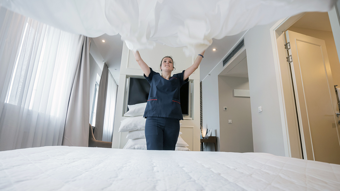 Young maid making the bed in hotel room.