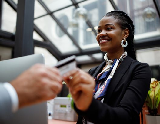 Women smiling at hotel reception desk receiving credit card payment.